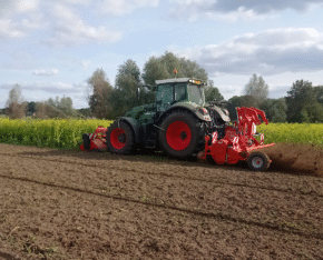 Tractor bewerkt een akker naast een veld met gele bloemen.