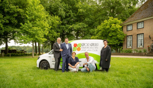 Vijf mensen poseren bij een bestelbus met het logo ‘Goei Gerei Streekproducten Land van Cuijk’, naast een boerderij en groene bomen.