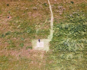 Luchtfoto van een grasveld met in het midden een persoon die op een gemarkeerd vierkant staat.